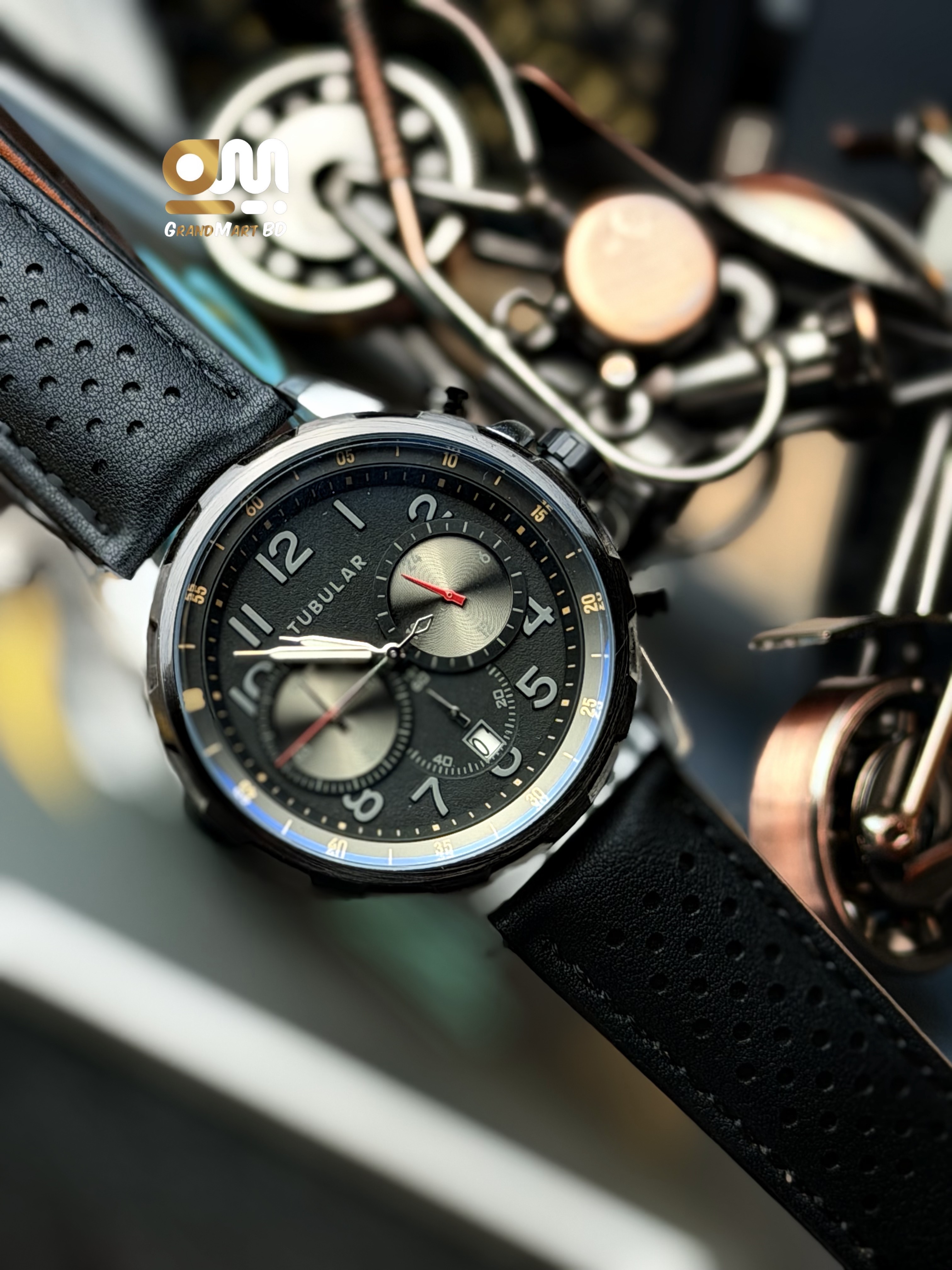 Tubular featuring a black chronograph-style textured dial with numeric markers and a perforated black leather strap._img_3