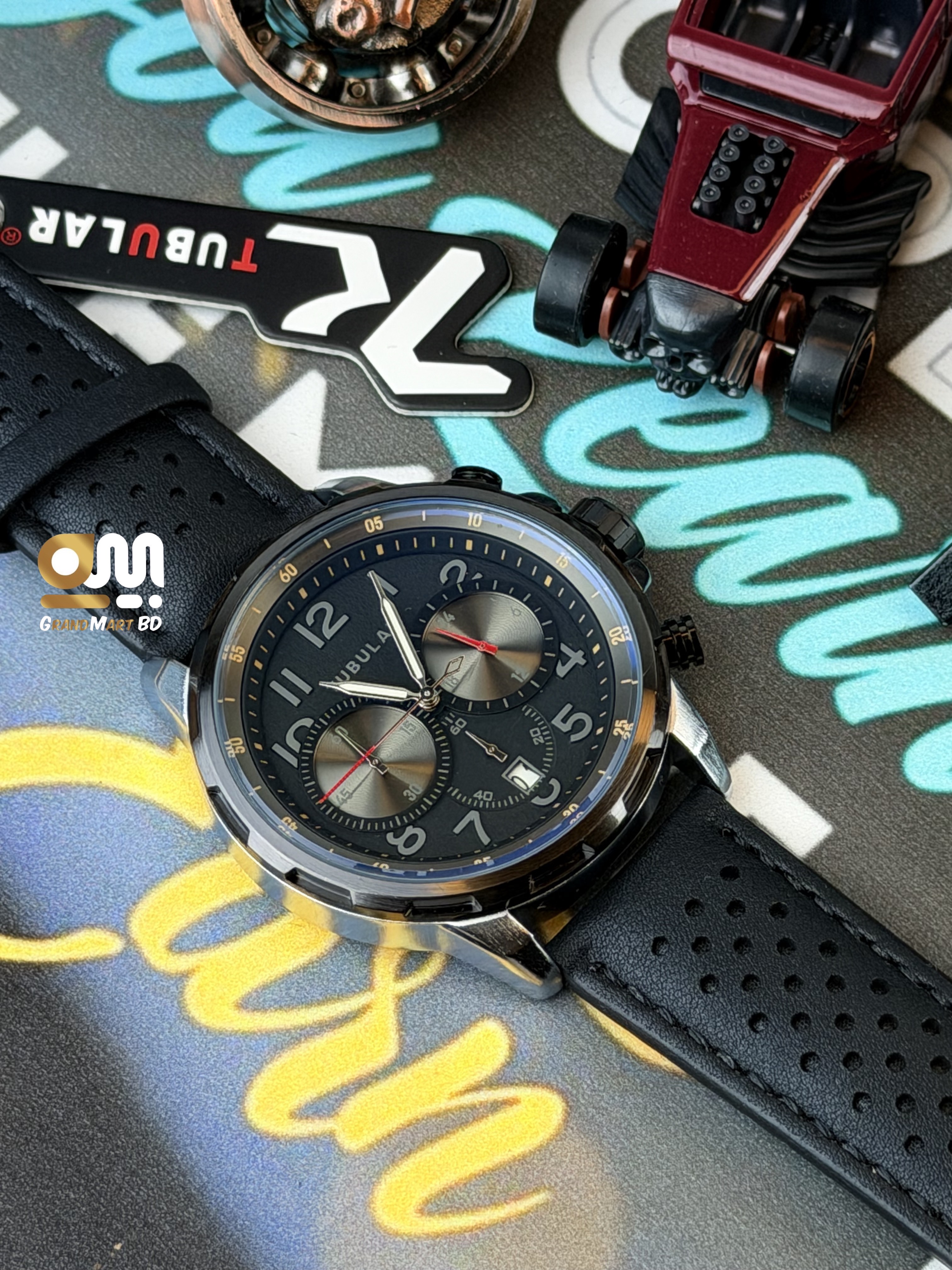 Tubular featuring a black chronograph-style textured dial with numeric markers and a perforated black leather strap._img_2